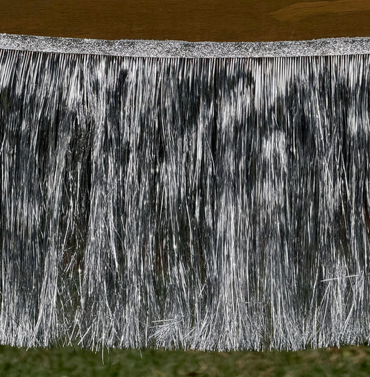 Silver tinsel fringe trim hanging from a glittery silver top band, shown against a background with a wooden surface above and grass below.