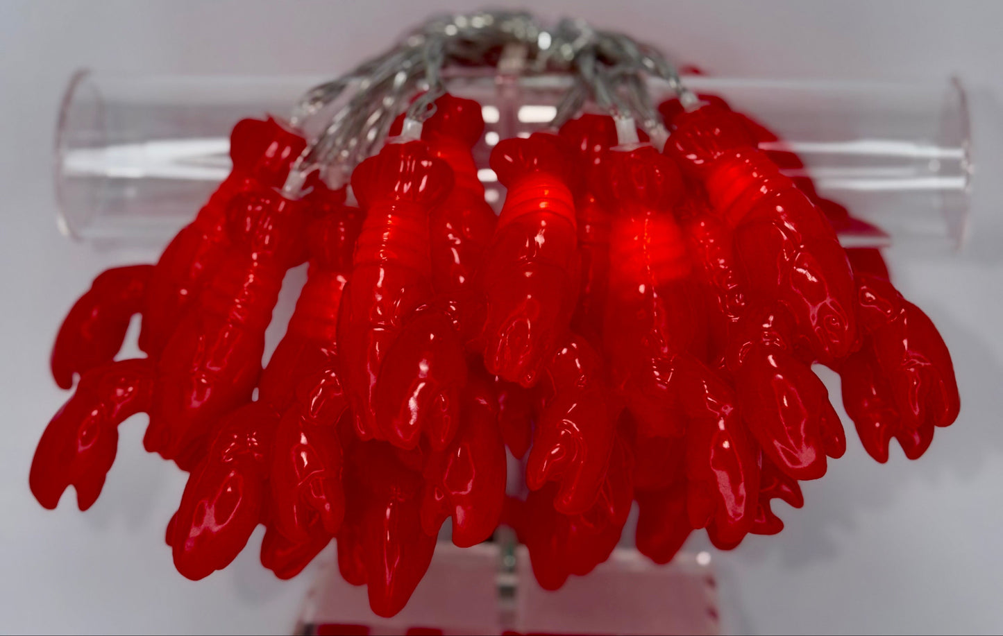 A cluster of bright red lobster-shaped beads or charms attached to a silver-toned ring, displayed on a clear cylindrical stand against a plain light background.