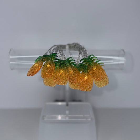 A pair of gold and green pineapple-shaped earrings displayed on a clear acrylic stand against a neutral gray background.