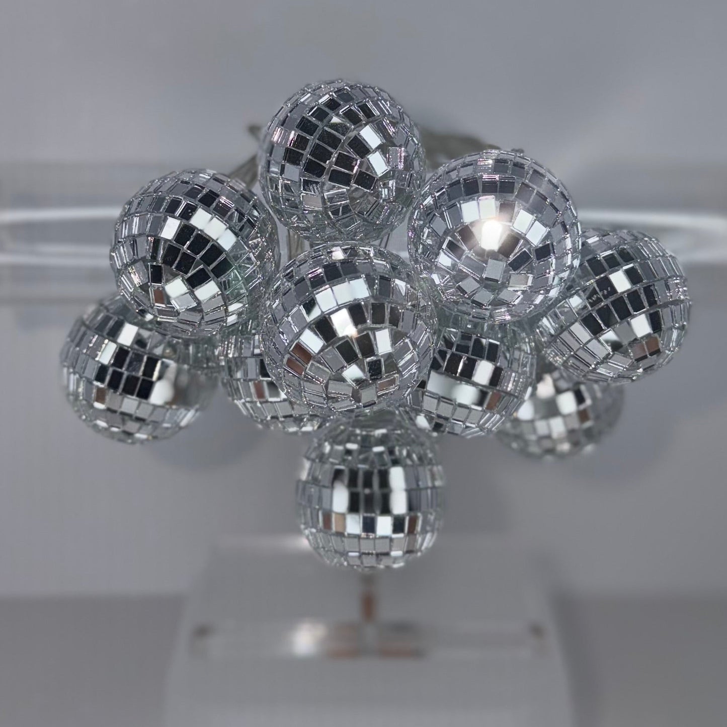 A cluster of small silver disco ball hair clips arranged on a clear plastic display stand against a light gray background.