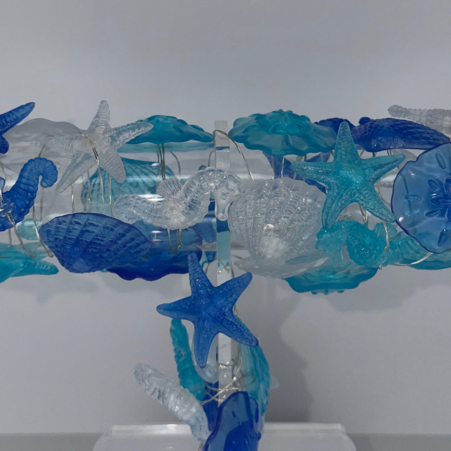A decorative blue and clear glass or acrylic column featuring starfish, seahorse, shell, and coral-like sea life motifs, photographed against a plain light gray background.