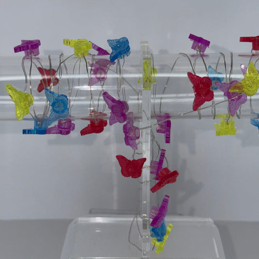 A clear acrylic spiral display stand holding multiple colorful translucent clip-like ornaments in red, yellow, blue, and purple, photographed against a plain light background.