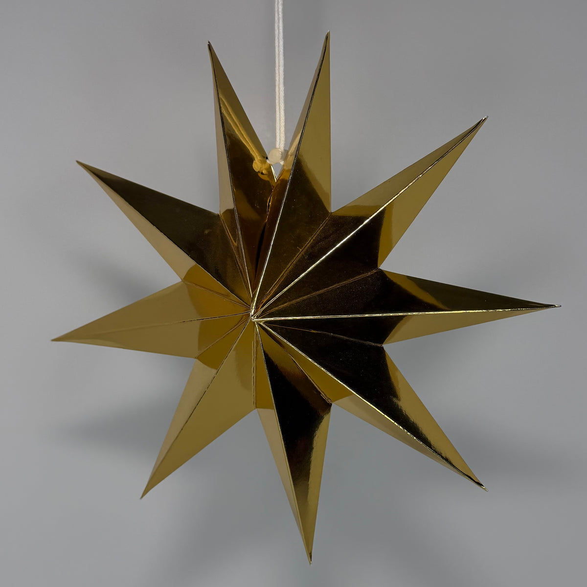 A metallic gold 11-pointed star hanging ornament suspended by a white string, shown against a neutral gray background.