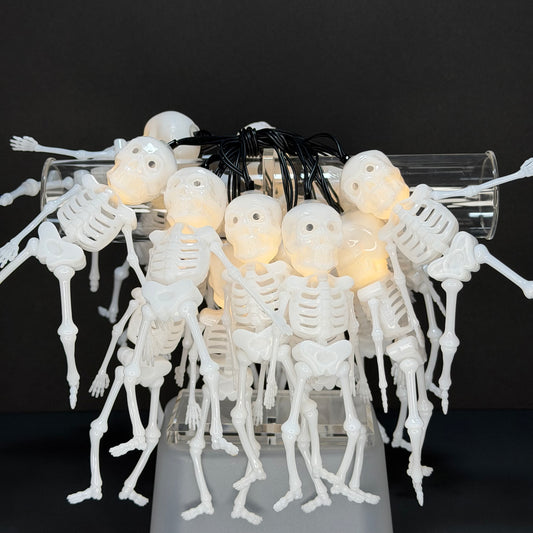 White plastic skeleton string lights with glowing warm-white LED heads, arranged in a clear cylindrical tube on a dark background.