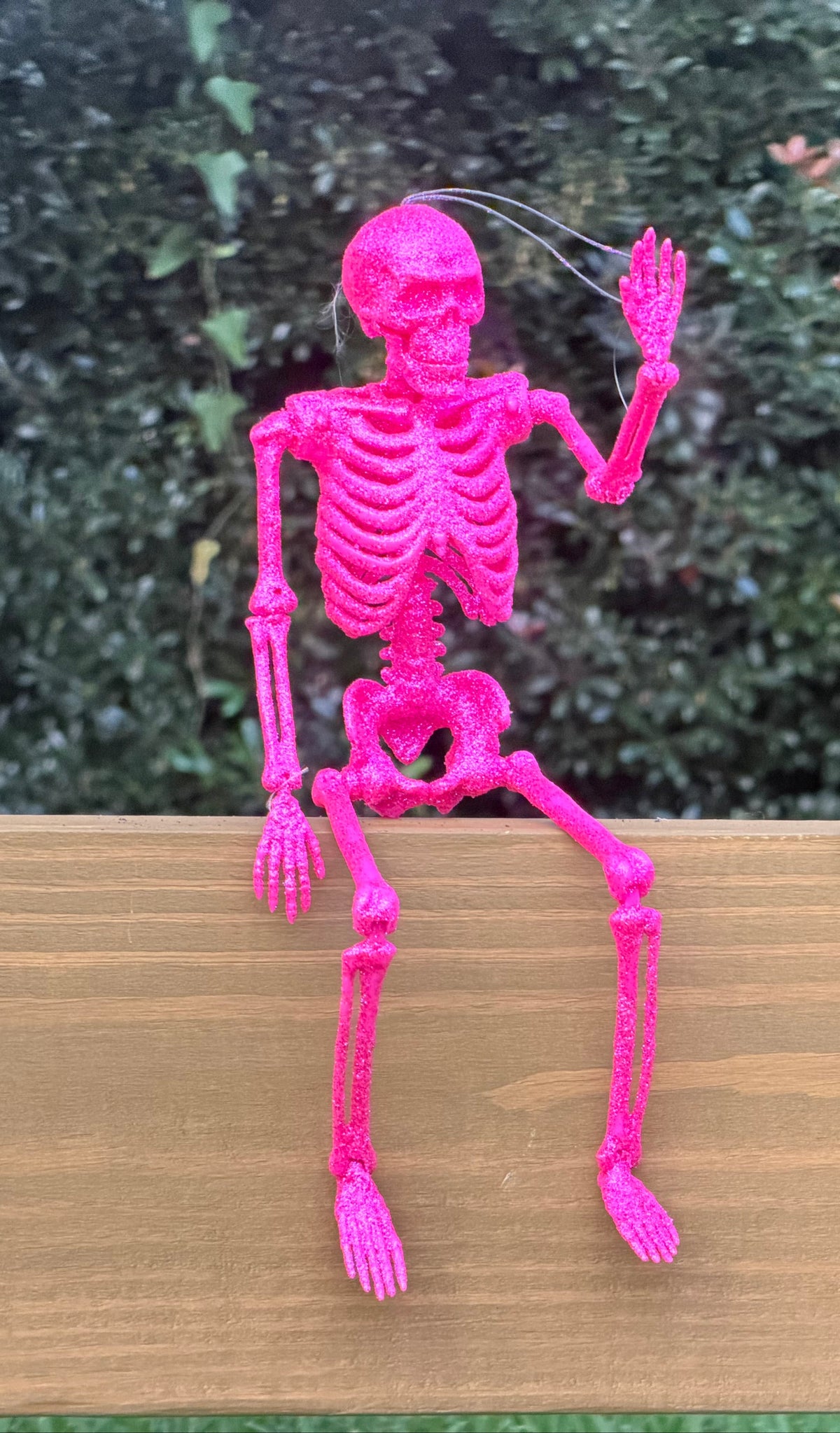 Hot pink and glitter skeleton posed sitting on a center rail waving in the daytime