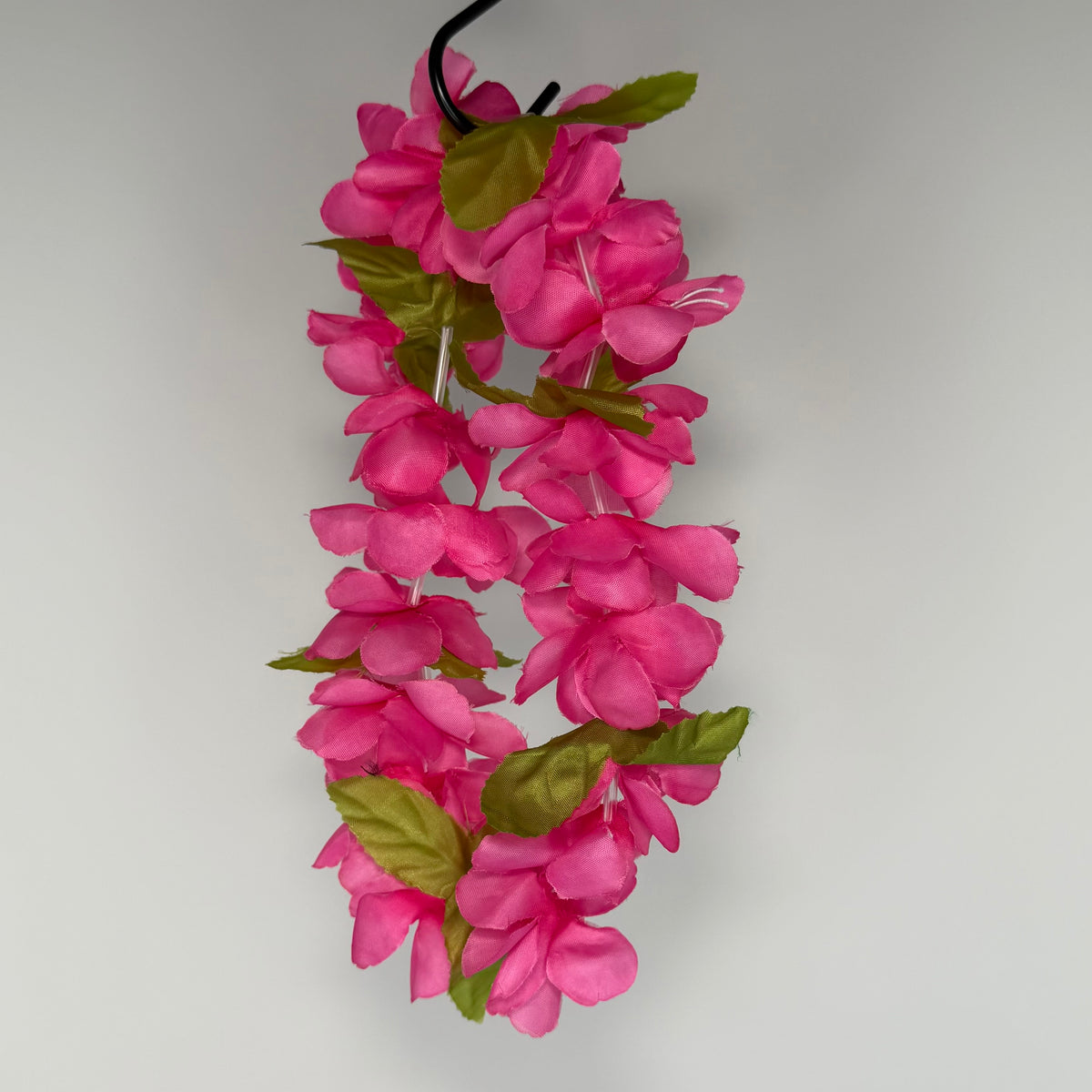 A pink flower lei or headpiece with bright pink blossoms and green leaves hanging against a plain light gray background.