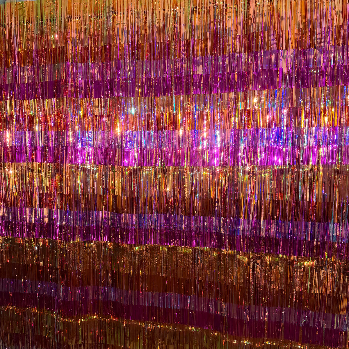 Fire Opal Fringe Backdrop hung outdoors showing alternating stripes of gold, copper, and magenta purple metallic fringe