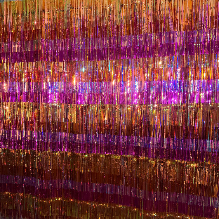 Fire Opal Fringe Backdrop hung outdoors showing alternating stripes of gold, copper, and magenta purple metallic fringe