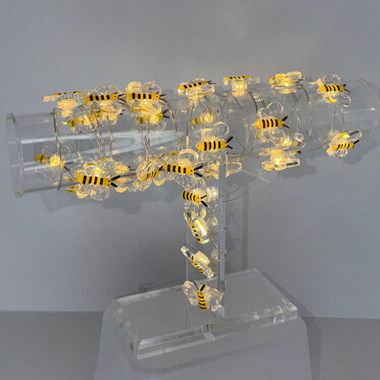 A modern wall-mounted light fixture with a clear acrylic cylindrical body decorated with numerous small yellow and black bumblebee figures, casting a warm glow against a plain light gray wall.