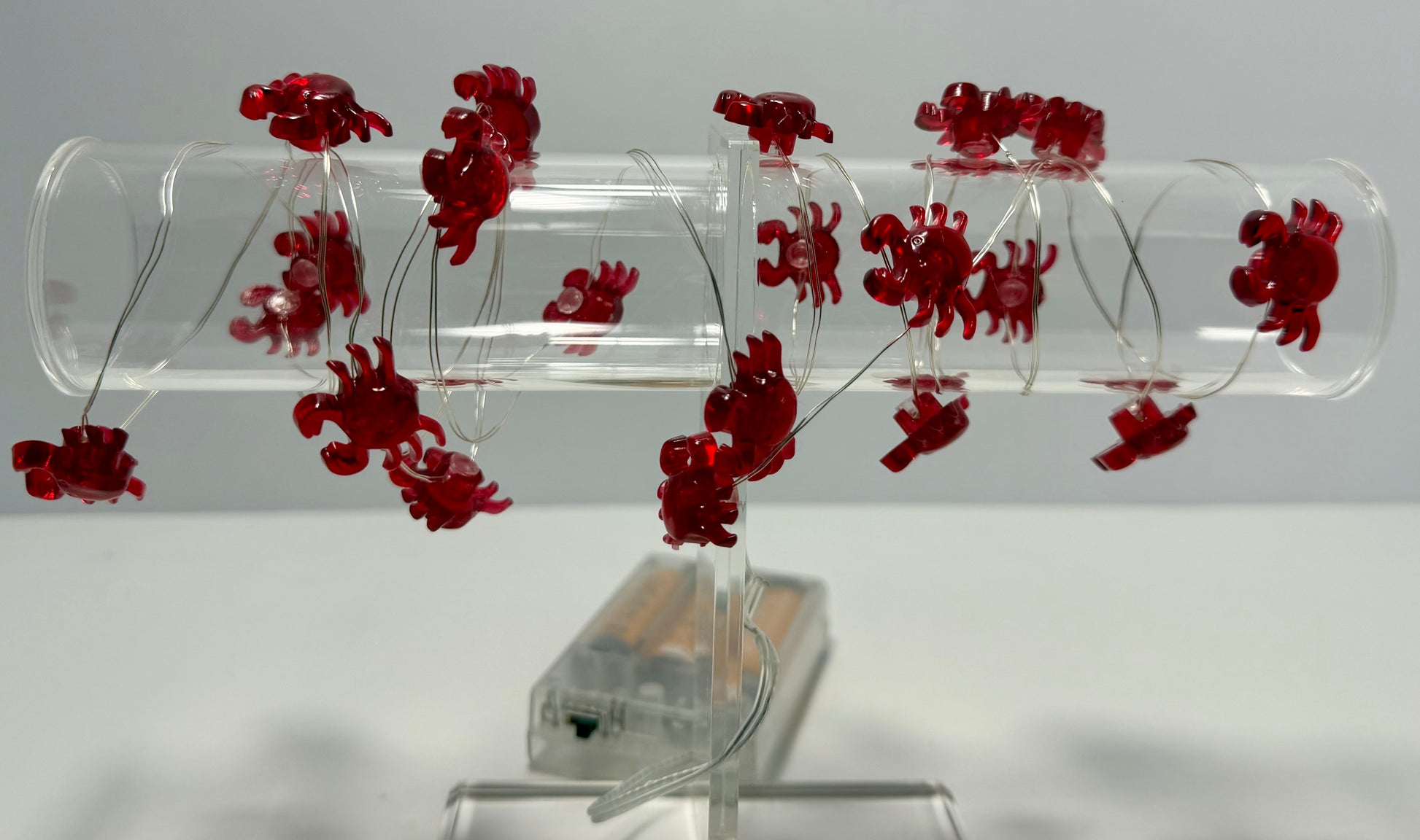 A clear acrylic spiral tube toy with multiple small red crab-shaped charms attached along the inner spiral, displayed on a clear stand against a light gray background.