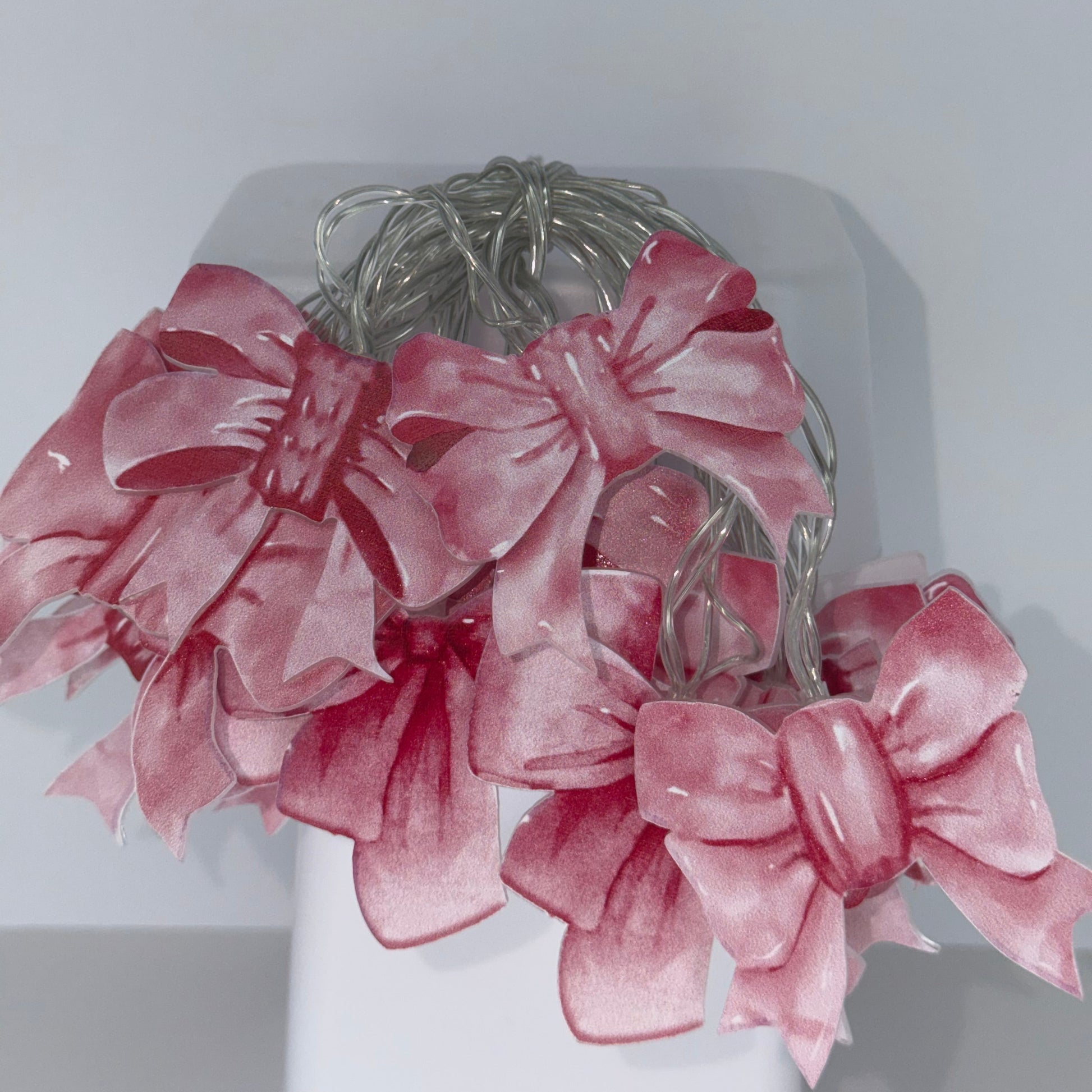 A bundle of pink sheer ribbon bows with silver wire loops, displayed on a white geometric stand against a light gray background.