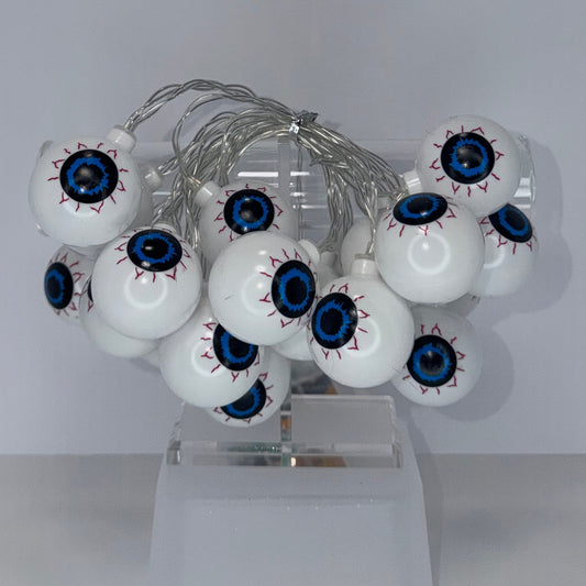 A cluster of white globe-shaped decorative bulbs with detailed blue, black, and red eyeballs, mounted on a clear plastic stand against a plain light gray background.