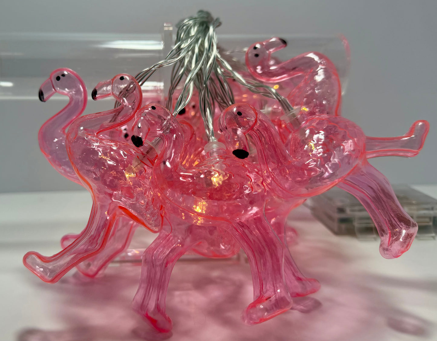 Pink flamingo-shaped string lights with a translucent plastic body and warm white internal bulbs, shown with the wire harness on a light gray background.