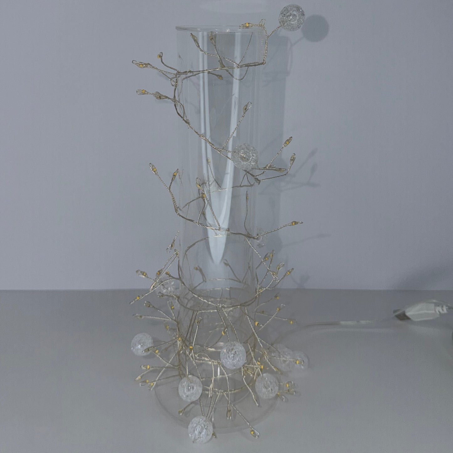 A white wall-mounted decorative light fixture with a curved backplate and branching wireframe arms holding clear globe bulbs, shown against a plain light gray wall.