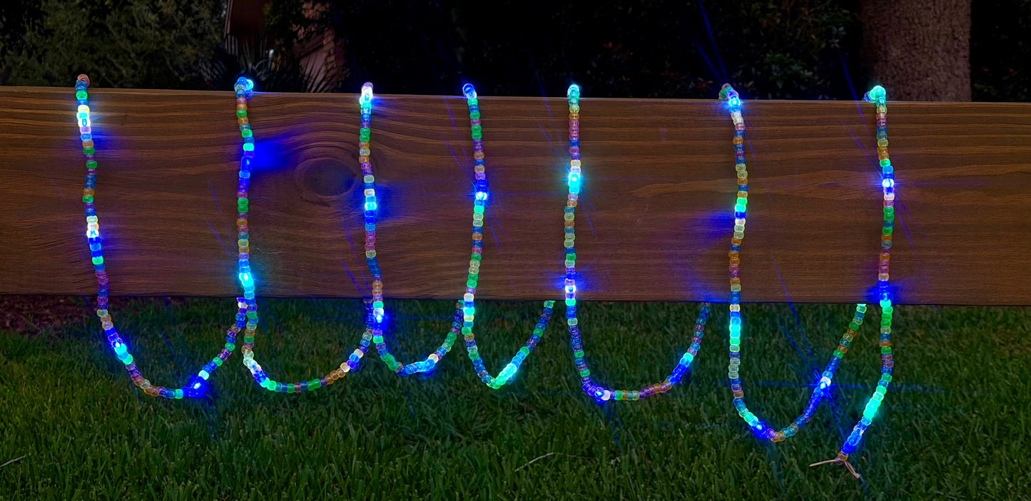 Multicolor LED bead garland lights draped in U-shapes over a wooden fence on a grassy lawn at night.