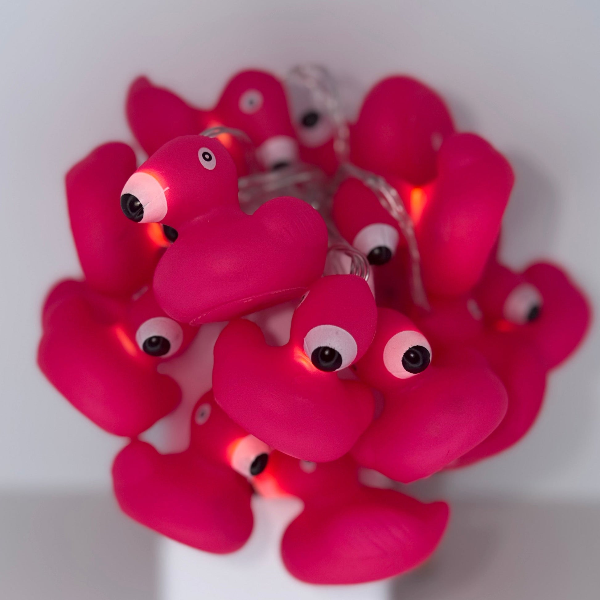 A cluster of pink flamingo-shaped string lights with glowing warm white bulbs, displayed on a white stand against a plain light gray background.