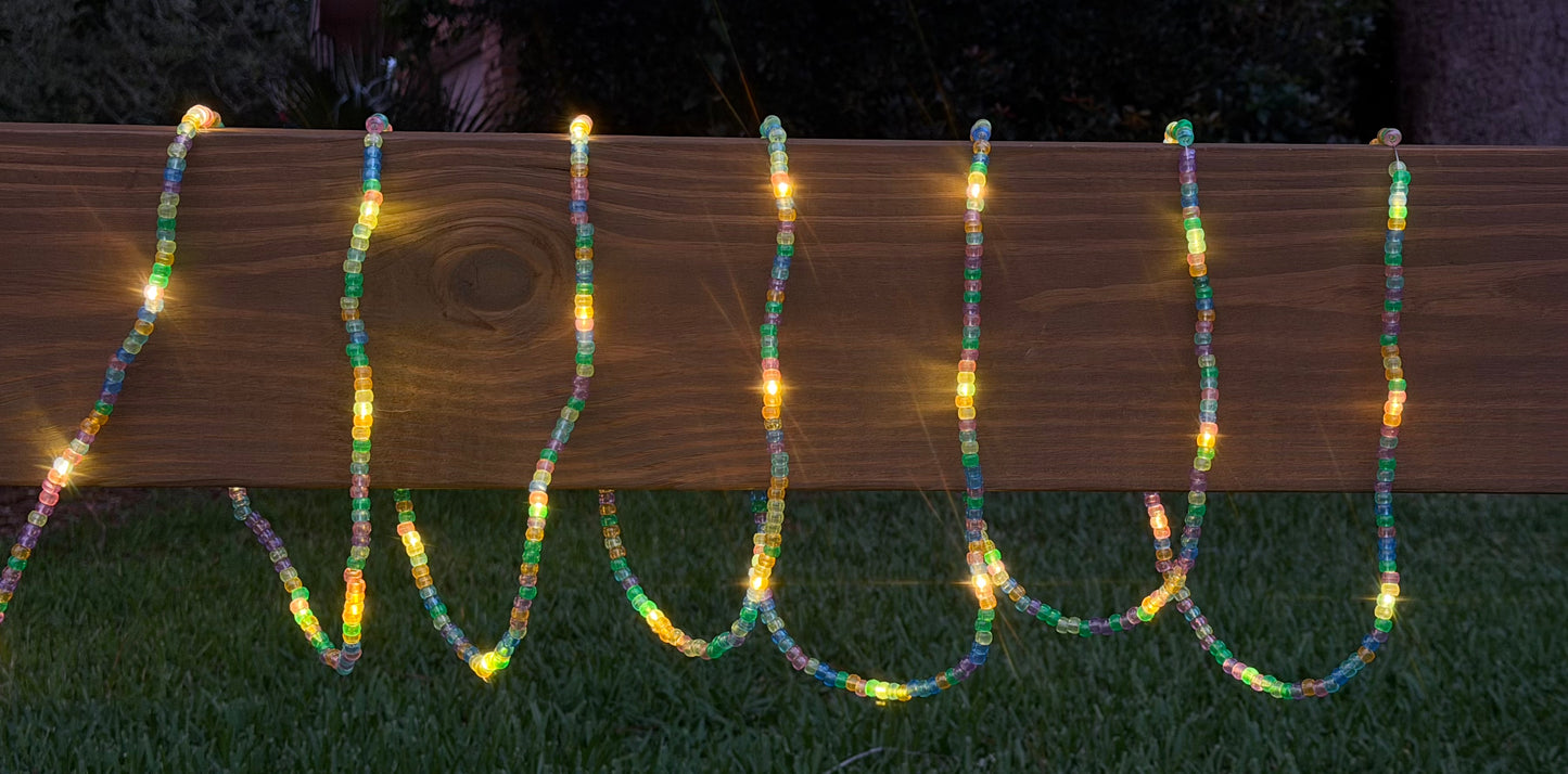 Multicolor LED bead garland lights draped over a wooden fence on a lawn at night.