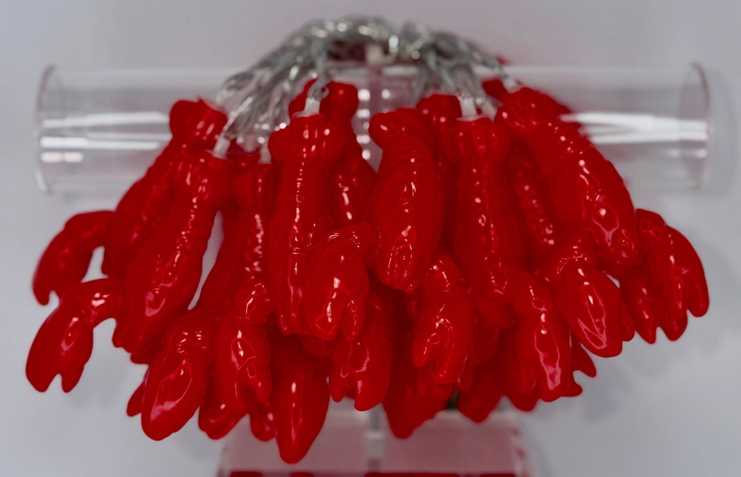 A cluster of glossy red lobster-shaped jewelry pieces attached to a clear acrylic display stand against a plain light background.