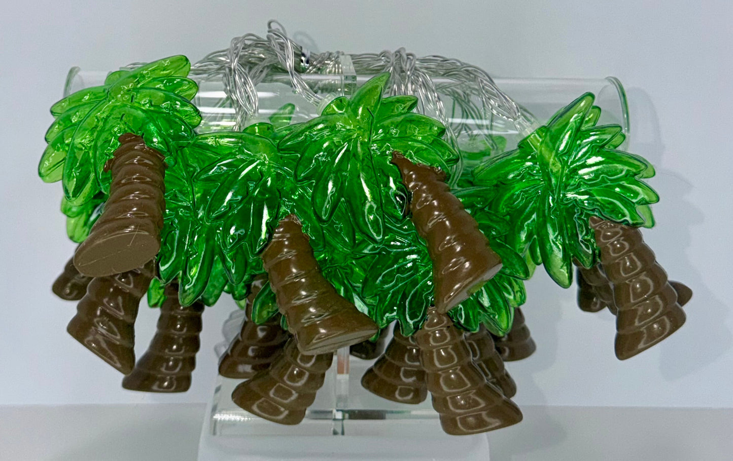 A set of small green and brown palm tree-shaped accessories displayed on a clear acrylic stand against a plain white background.