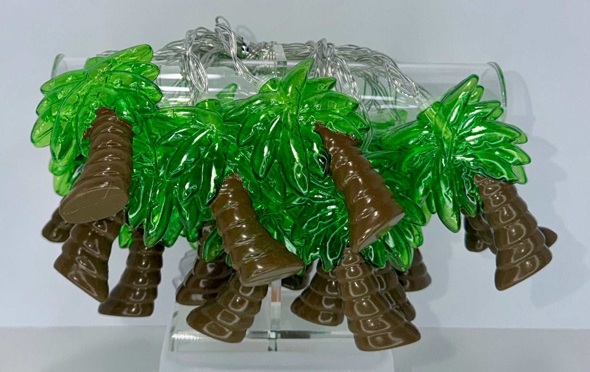 A set of small green and brown palm tree-shaped accessories displayed on a clear acrylic stand against a plain white background.