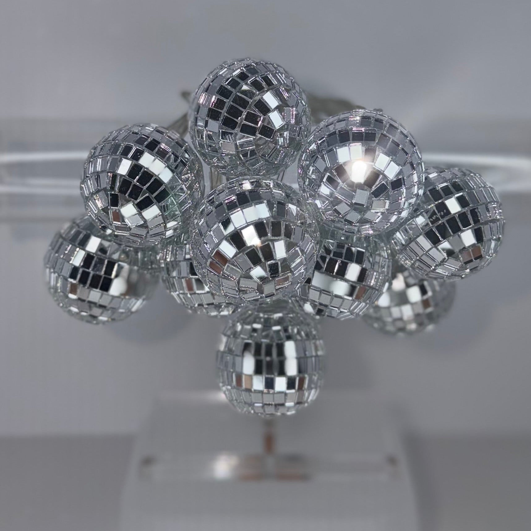 A cluster of small silver disco ball hair clips arranged on a clear plastic display stand against a light gray background.