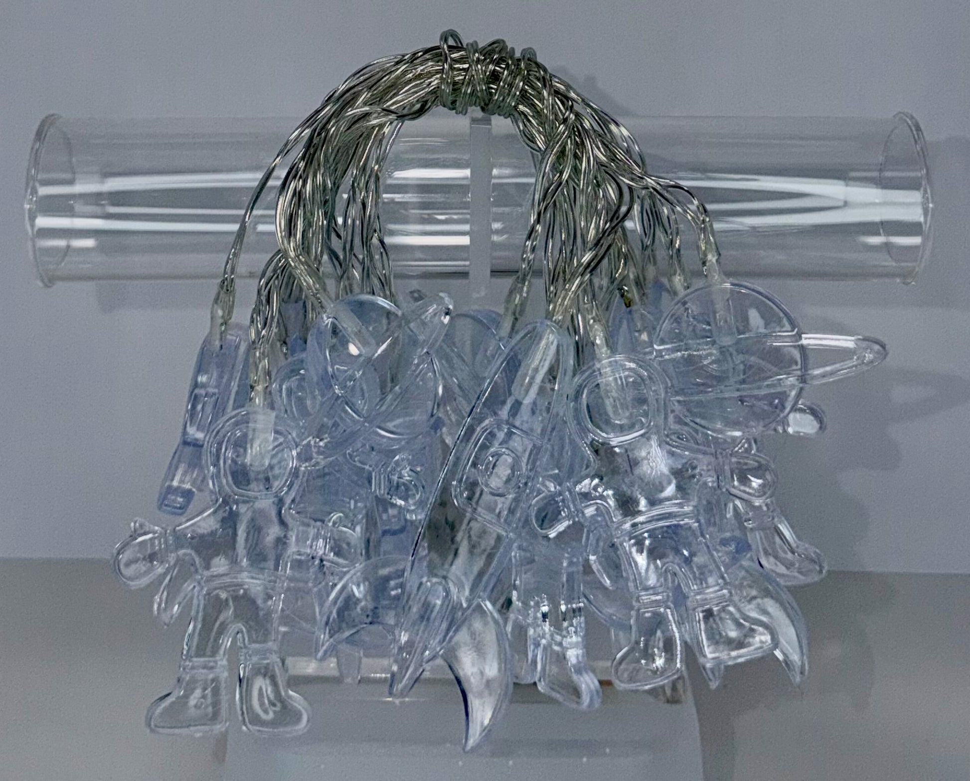 Clear plastic Christmas ornaments shaped like animals, hanging from a bundle of silver wire lights, displayed in front of a clear cylindrical stand against a light gray background.