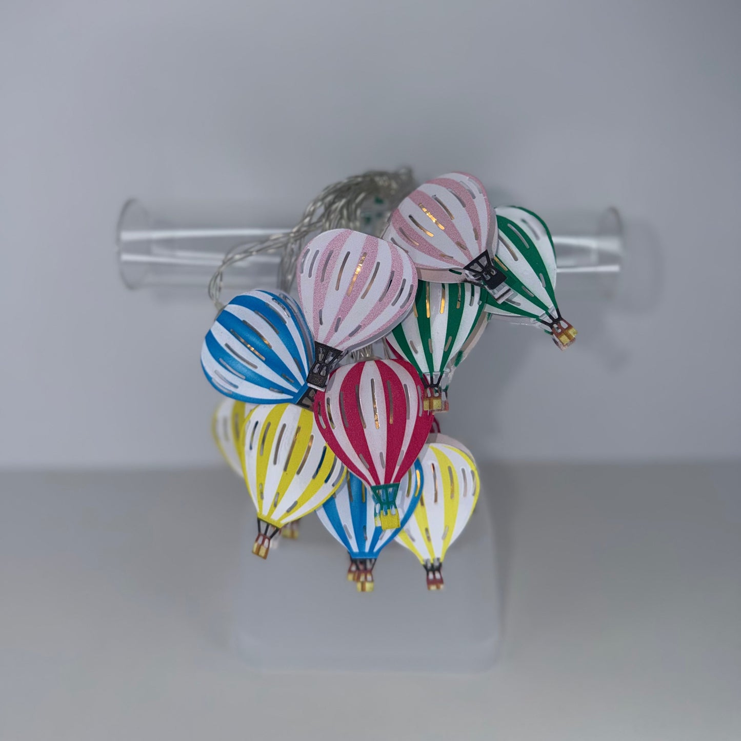 A cluster of small hand-painted hot air balloon ornaments in various colors including pink, blue, green, yellow, and red, displayed on a clear acrylic stand.