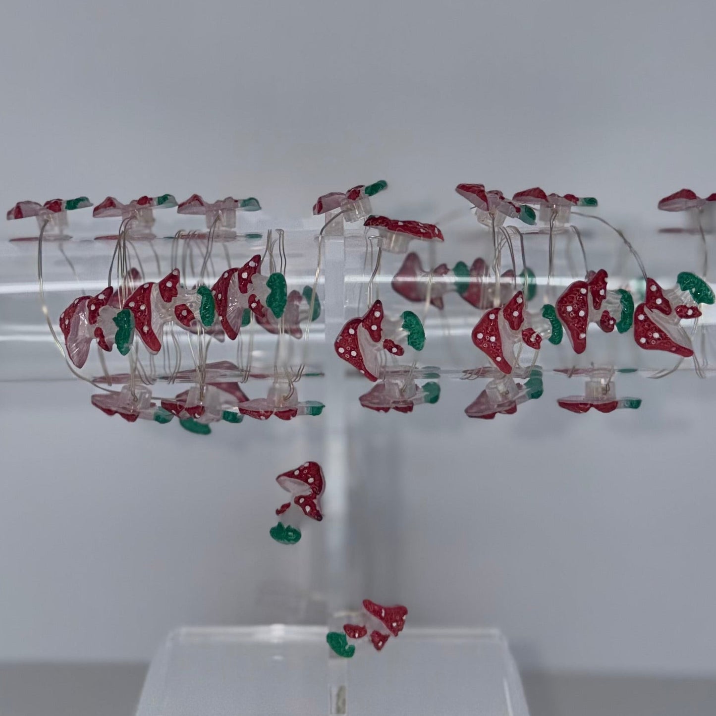 A clear acrylic jewelry display stand holding multiple pairs of dangling earrings with red and green bead or crystal details, photographed against a plain light gray background.