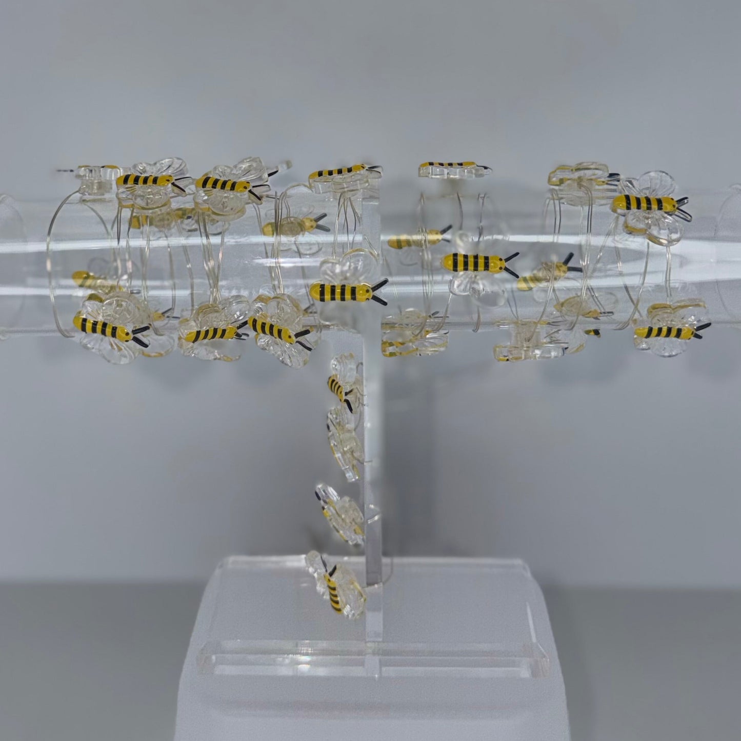 A clear acrylic T-shaped display stand holding multiple small yellow-and-black striped artificial bees, photographed against a plain light gray studio background.