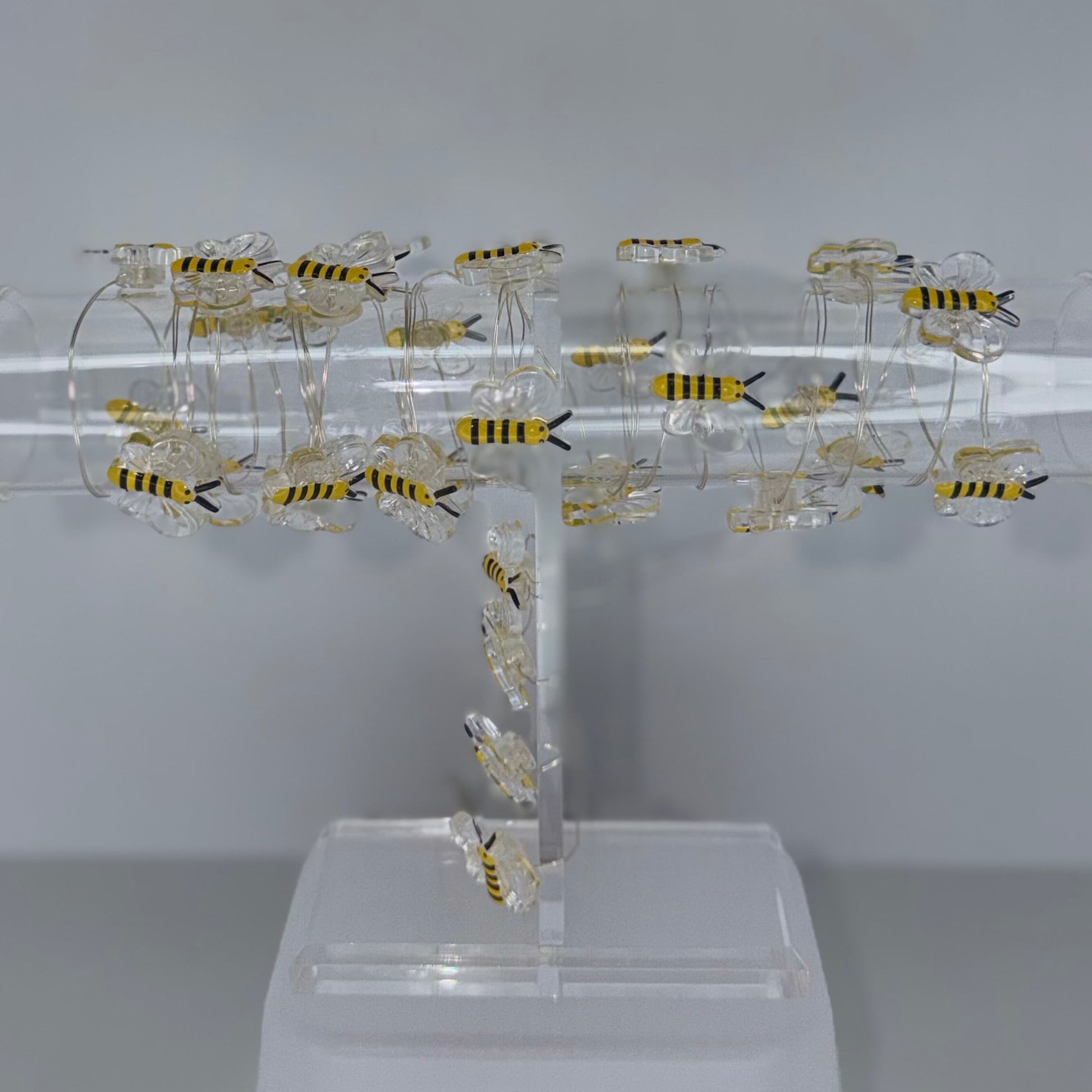 A clear acrylic T-shaped display stand holding multiple small yellow-and-black striped artificial bees, photographed against a plain light gray studio background.