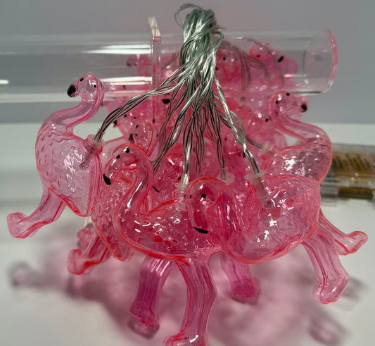 Pink translucent flamingo-shaped string lights with a silver wire, photographed on a white surface with a clear plastic tube in the background.