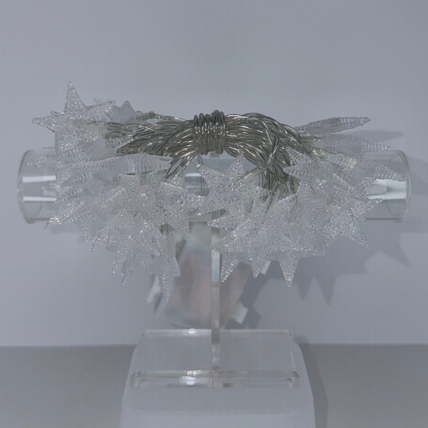 A modern wall-mounted light fixture with a sculptural, snowflake-like clear acrylic or glass design and a central metallic silver element, mounted on a white wall.