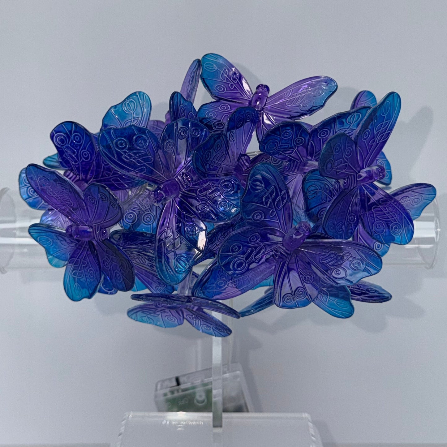 A cluster of translucent blue and purple butterfly-shaped wall lights mounted on a clear cylindrical holder against a plain light gray wall.