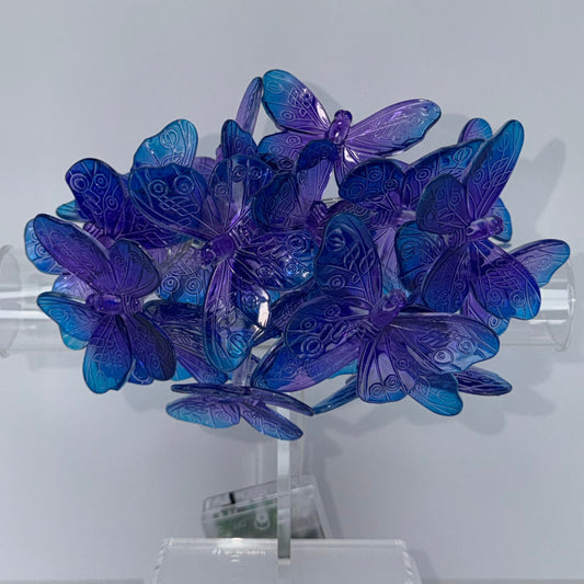 A cluster of translucent blue and purple butterfly-shaped wall lights mounted on a clear cylindrical holder against a plain light gray wall.