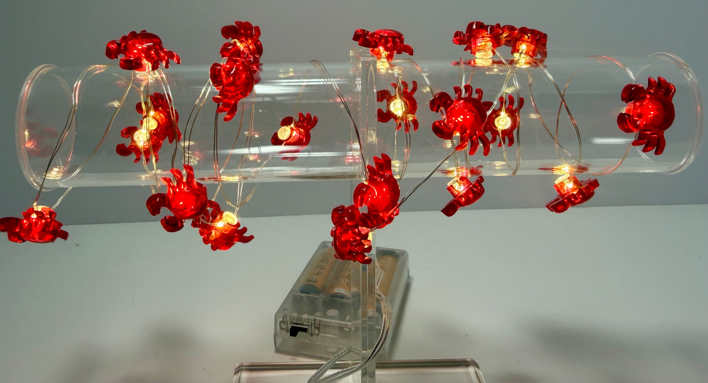 Red crab-shaped string lights with warm glowing bulbs, draped over a clear cylindrical acrylic tube on a white surface against a light gray background.