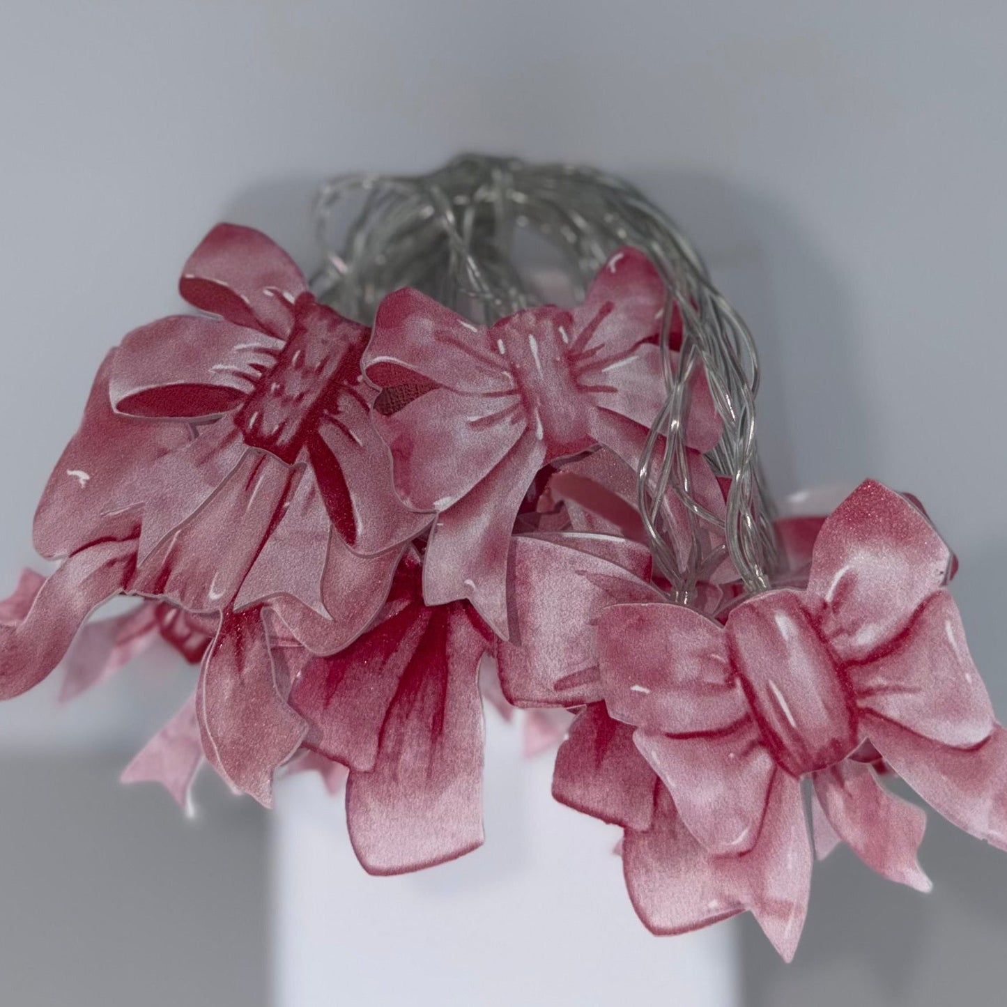 A pink satin bow headband with a sheer mesh backing and small clear rhinestones, displayed on a white stand against a neutral gray background.