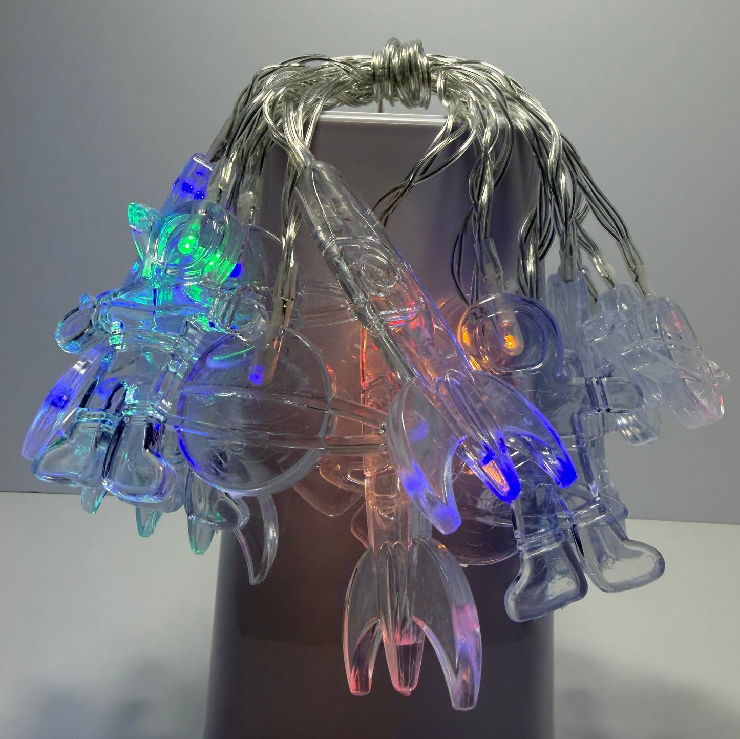 Multicolor LED clip-on string lights draped over a dark cylindrical stand, showing clear plastic clips glowing with blue, green, and orange light against a plain gray background.