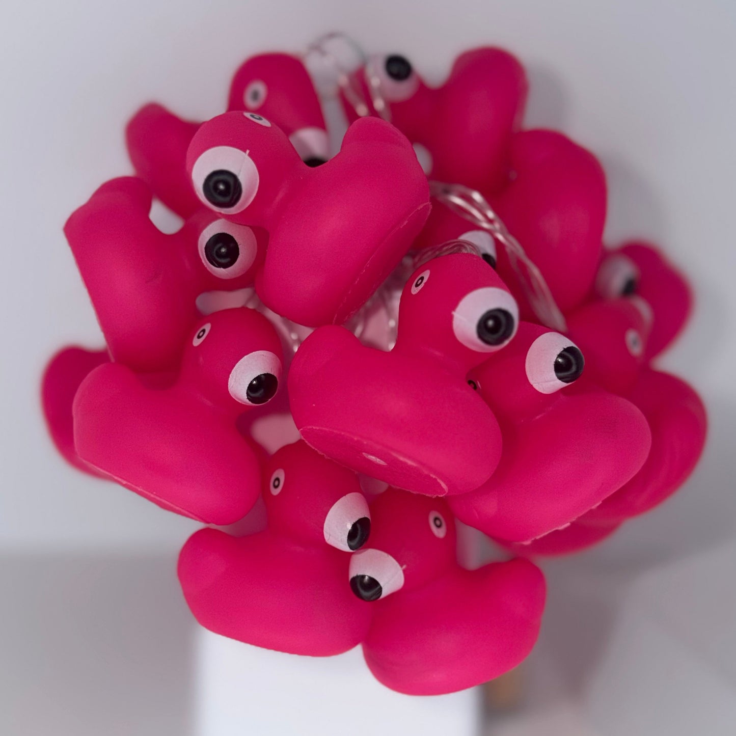 Bright pink novelty string lights shaped like ducklings with large cartoon eyes, shown draped over a white stand against a plain light background.