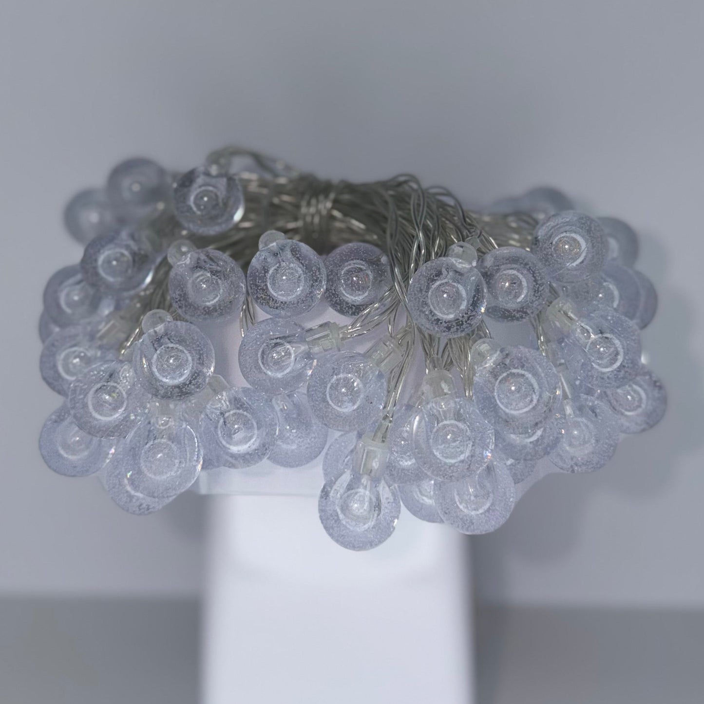 A cluster of small clear teardrop-shaped glass beads on a white display stand against a plain light gray background.