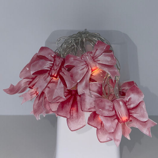 A pink silk flower arrangement with a warm orange glow from hidden fairy lights, displayed on a white rectangular block against a minimalist gray background.
