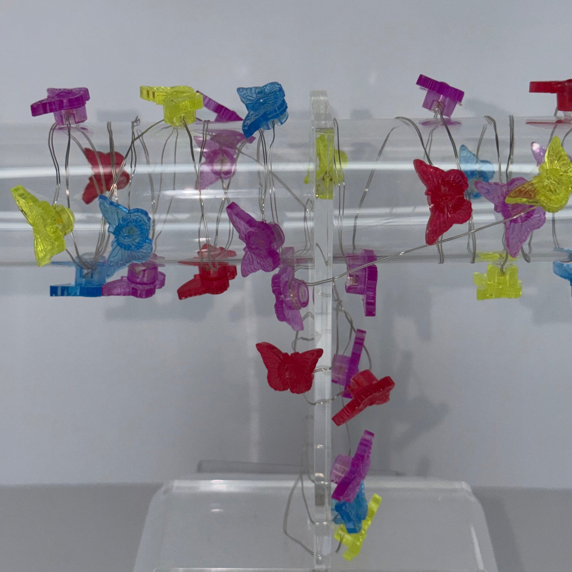 A clear acrylic spiral display stand holding multiple colorful translucent clip-like ornaments in red, yellow, blue, and purple, photographed against a plain light background.