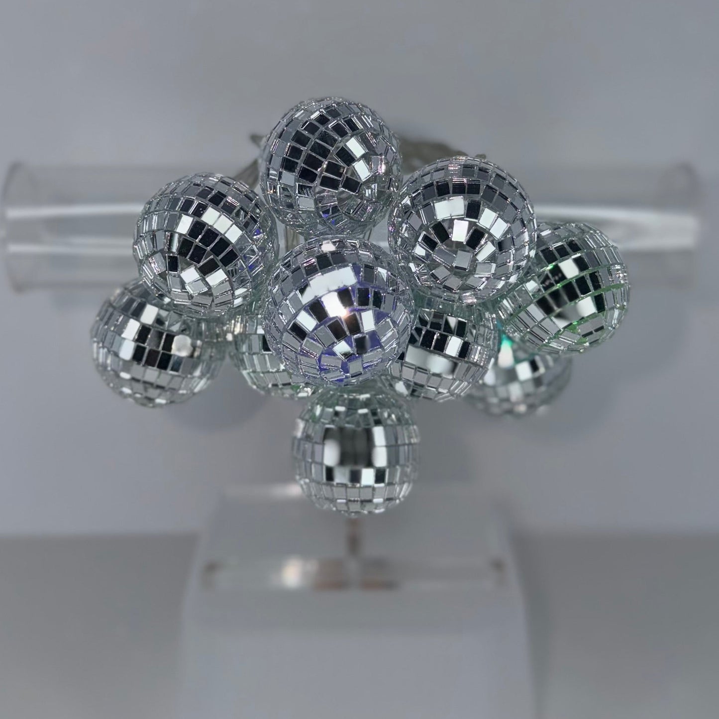 A cluster of small mirrored disco ball ornaments displayed on a clear stand against a light gray background.