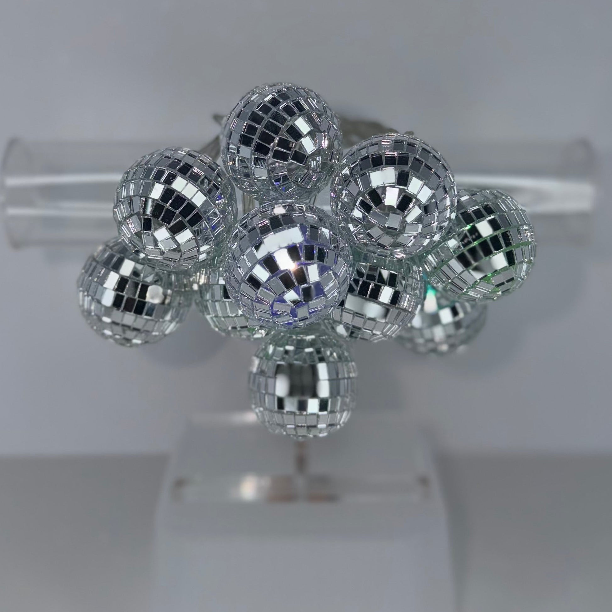 A cluster of small mirrored disco ball ornaments displayed on a clear stand against a light gray background.