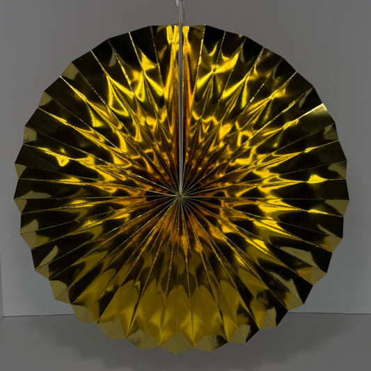 A round, metallic gold paper fan decoration with a pleated, accordion-like design, hanging against a neutral gray background.
