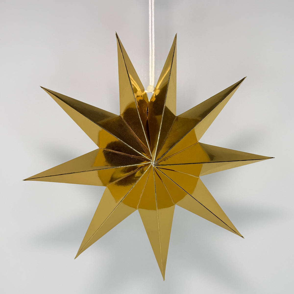 A metallic gold 12-pointed star hanging ornament suspended by a thin white cord against a neutral light gray background.