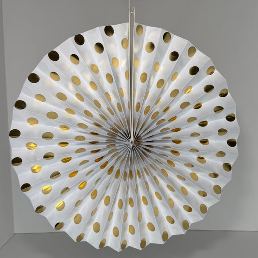 A white paper fan decoration with metallic gold polka dots, hanging against a neutral gray background.