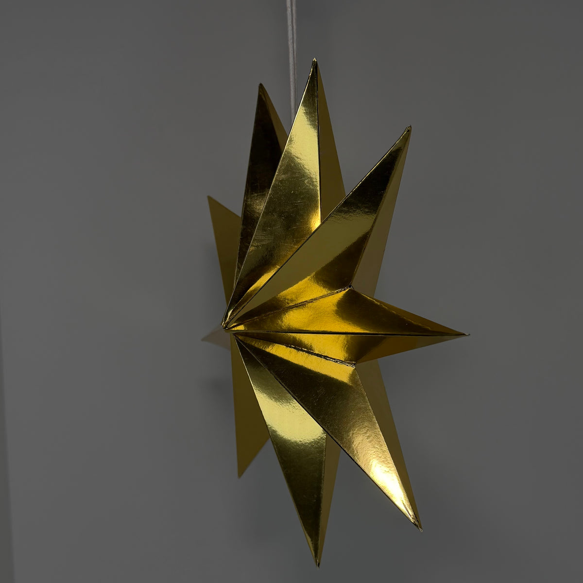 A metallic gold hanging star ornament with a reflective, crinkled texture, suspended against a plain gray background.