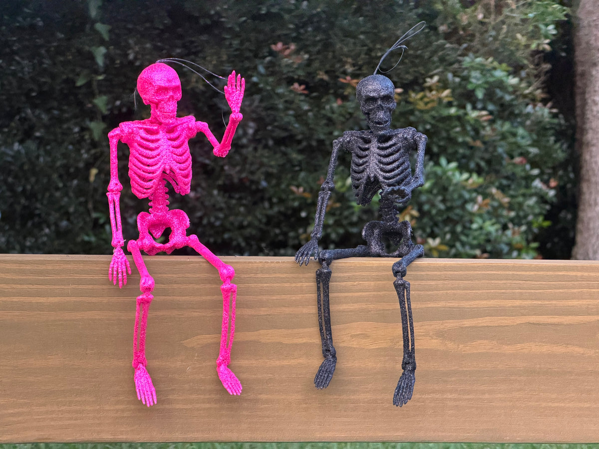 Hot pink and black glitter skeletons posed sitting on a center rail waving in the daytime
