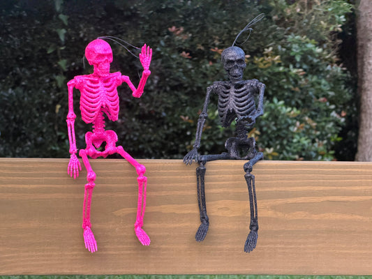 Hot pink and black glitter skeletons posed sitting on a center rail waving in the daytime