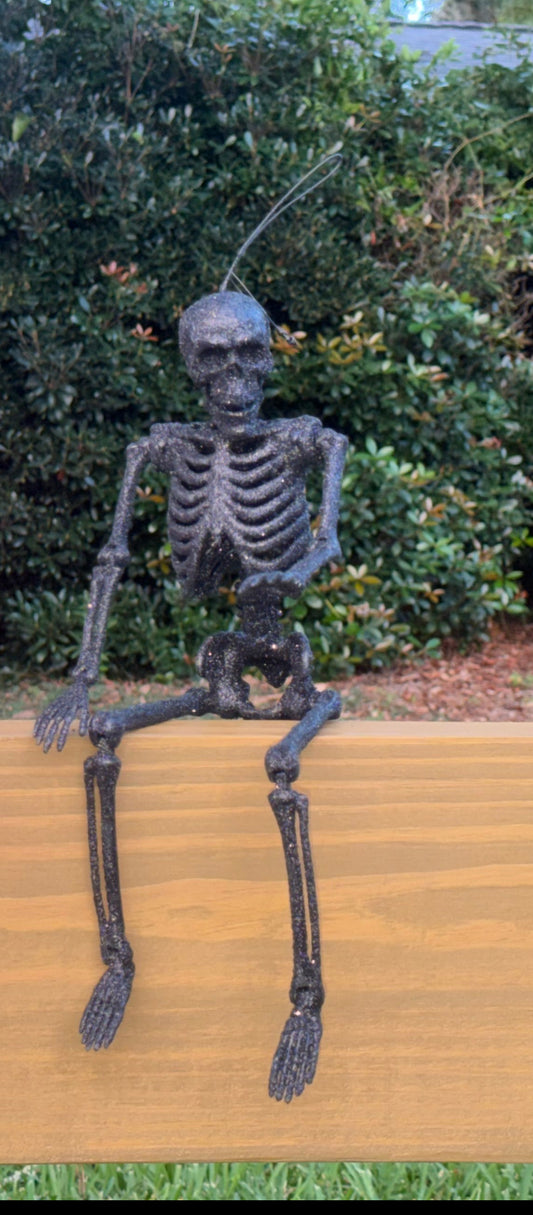 Black glitter skeletons posed sitting on a center rail waving in the daytime